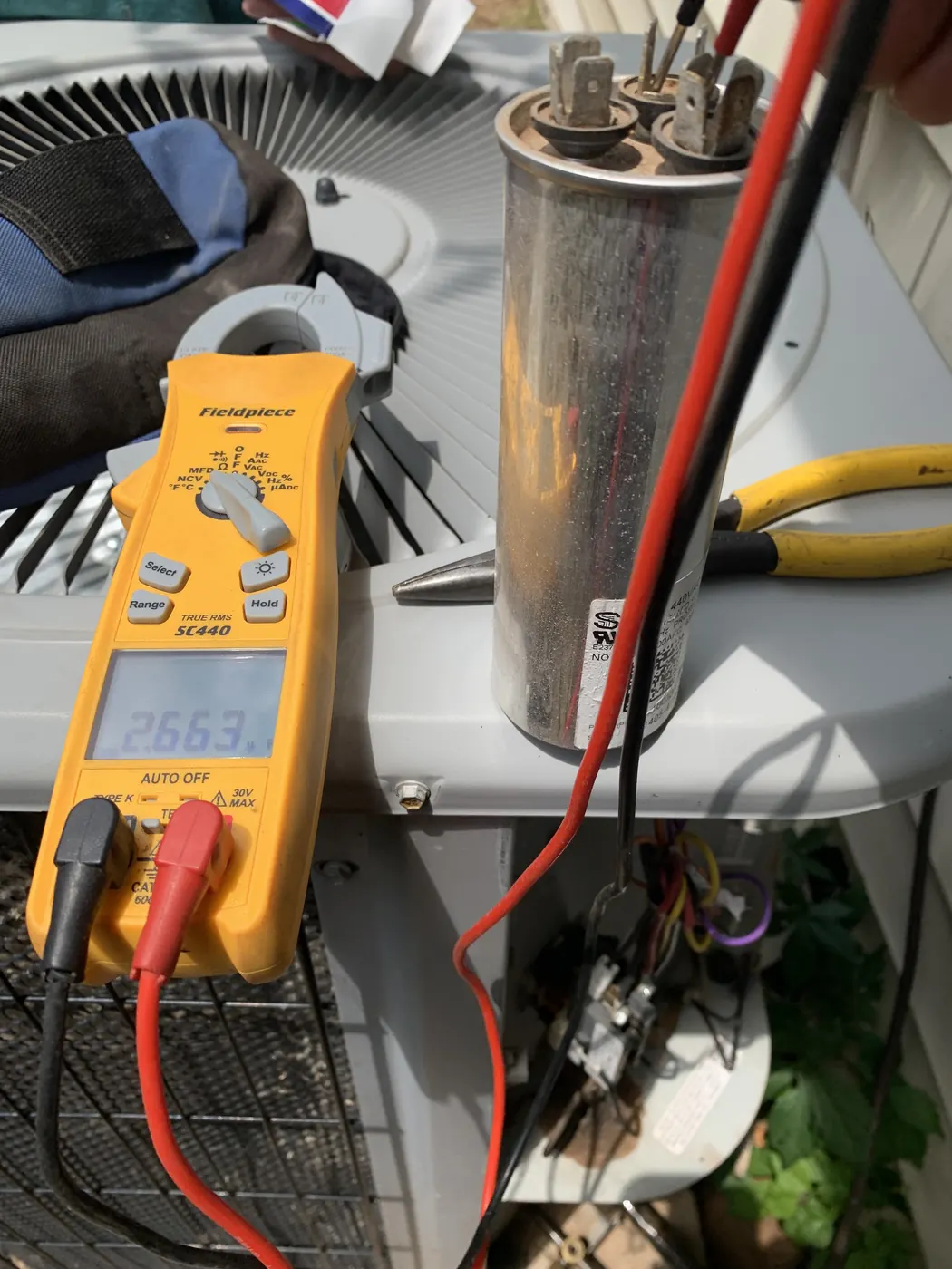 Testing a capacitor with a multimeter during an air conditioning repair