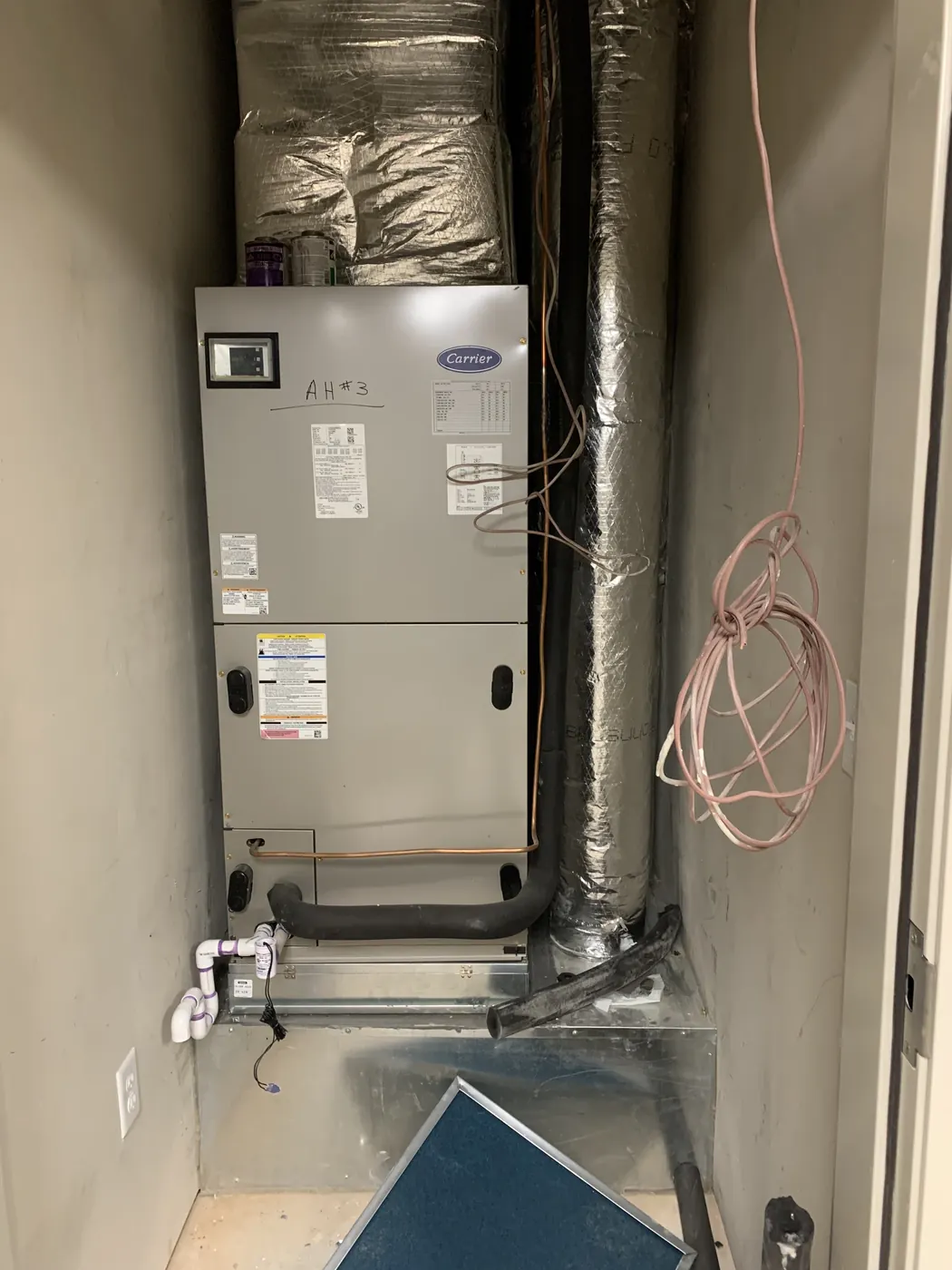 An air handler installed in a home utility closet with flex duct connections